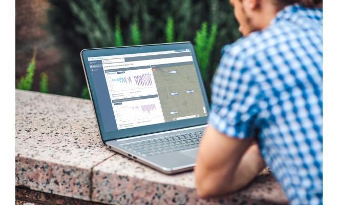 Man leaning on wall looking at laptop with data monitoring software