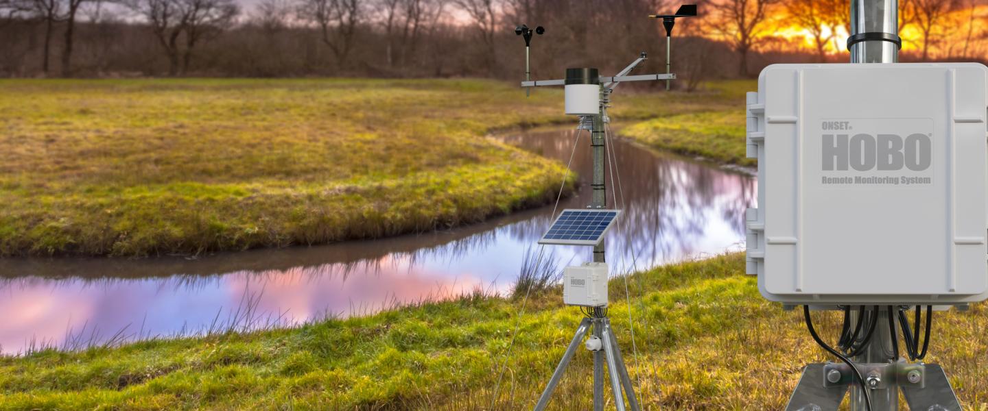 HOBO RX3000 deployed in a field with a river running through it with the sun setting in the background